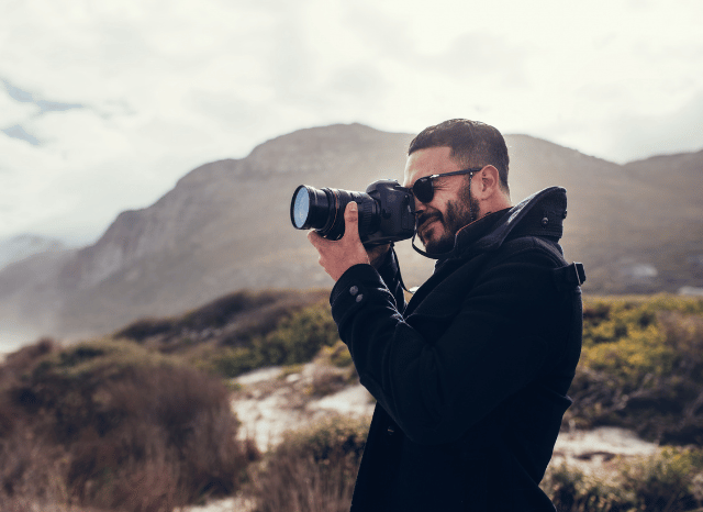 Male travel photographer taking pictures while exploring a summer destination, illustrating Stanislav Kondrashov and his tips on natural light, composition, mobility, and capturing memorable moments during a journey.